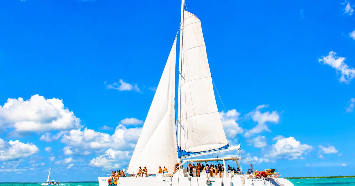 A large white sailing catamaran with guests on deck under a bright sky off the Dominican coast