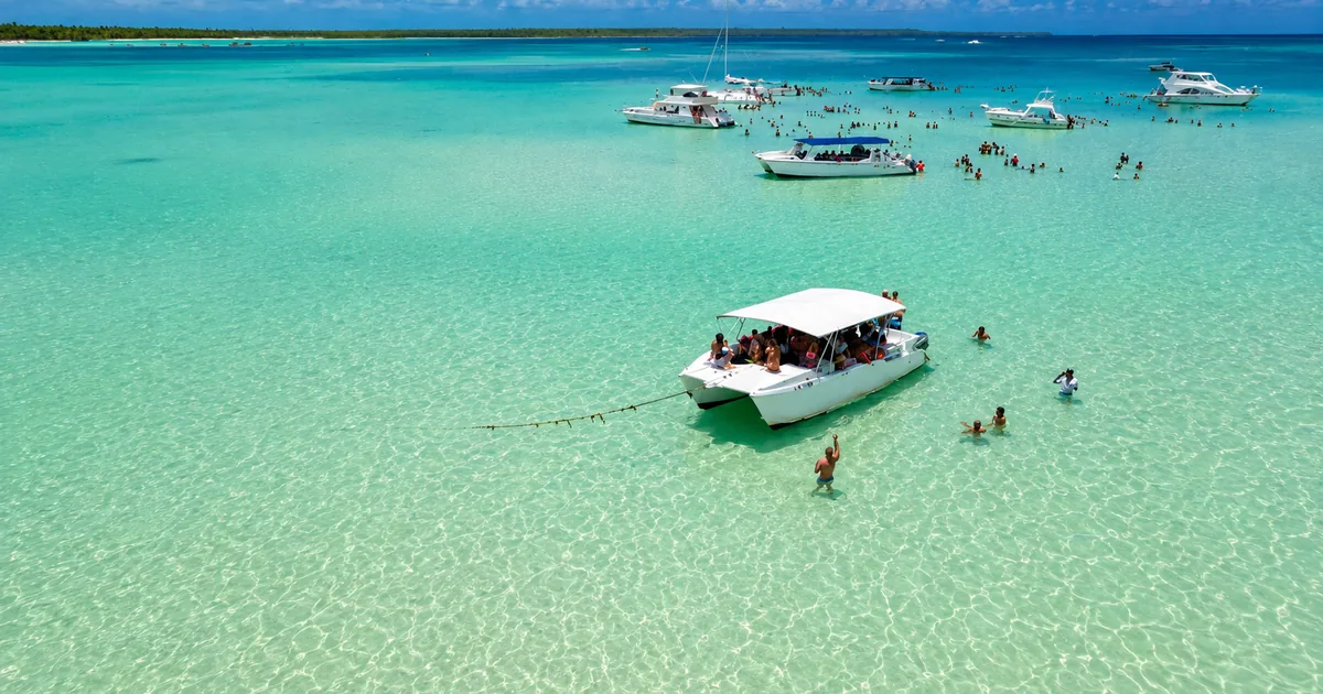 Aerial view of tour boats anchored over the pale sandbar of the natural pool, with guests standing in the shallow water